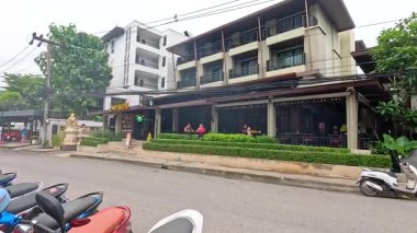 Ao Nang, Krabi 'de hareketli bir caddede motosikletler, yayalar ve bulutlu aydınlatma altında geçen bir minibüs var.