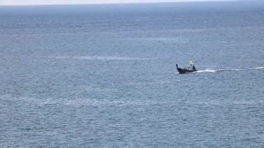 Uzun kuyruklu bir tekne Phuket, Tayland yakınlarında okyanusta süzülüyor, berrak gökyüzünün altında, huzurlu deniz yolculuğunu yakalıyor.