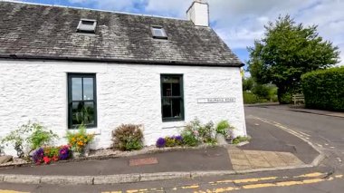 Dışarıda çiçekler ve yeşillik olan beyaz bir ev.