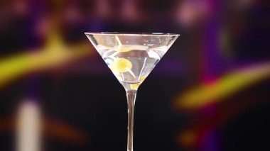 Loş bir barda bir martini bardağı zeytinlerle süslenir. Arka plan bulanık, içkiyi vurguluyor.