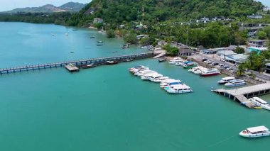 İnsansız hava aracı görüntüleri Phuket, Tayland 'da canlı bir marina yakalıyor. Şov tekneleri, bir rıhtım ve aydınlık gün ışığında yemyeşil bir çevre.