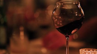 Kıvrımlı bir şarap kadehinin yakın plan çekimi loş, zarif bir yemek ortamında ortam ve karmaşıklığı yakalıyor.