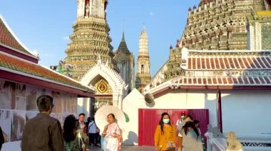 Turistler açık gökyüzünün altında Wat Arun 'da yürürler. Kamera karmaşık tapınak mimarisini ve hareketli etkileşimleri yakalar.