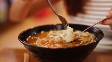 Bir insan çatal ve kaşıkla bir kase Vietnamlının tadına bakar. Ilık aydınlatma sıcak yemek atmosferini güçlendirir