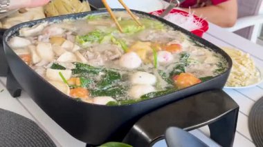 Canlı bir tencere, açık havada sebze, et ve balık köfteleriyle kaynıyor, ortak yemek ve ev yemeklerini ön plana çıkarıyor.