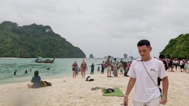 Turistler ve teknelerle dolu plaj sahnesi