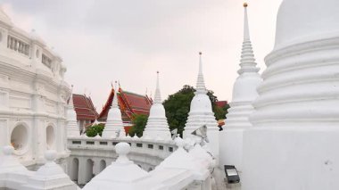 Bangkok 'taki Wat Prayurawongsawat' ın sakin bir sahnesinde ikonik beyaz pagoda ve geleneksel mimarisini gün ışığında sergiliyor.