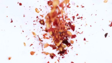 Kurutulmuş kırmızı biber taneleri beyaz bir yüzeye taşarak parlak bir ışık deseni oluşturur.