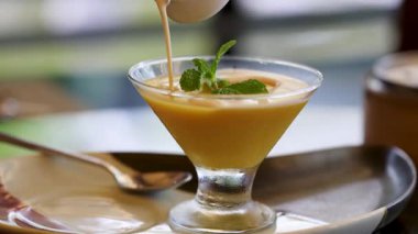 Kremalı bir sos bir bardakta Tayland tatlısının üzerine nazikçe dökülüyor ve zengin, davetkar bir sunum yaratıyor.