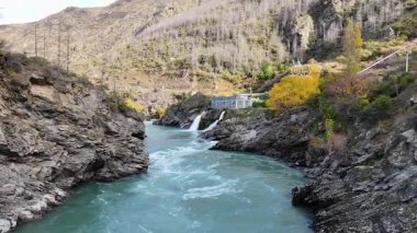İHA görüntüleri Orta Otago, Yeni Zelanda 'da sonbahar yeşillikleri arasında Kawarau Nehri ve hidroelektrik santralini yakalıyor.