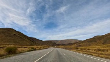 Tekapo Gölü 'nün engebeli arazisini kesen engin, bulutlu bir gökyüzü manzaralı bir yol. Huzurlu, geniş manzaraları yakalar