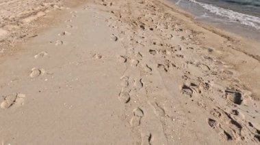 Okyanus dalgaları yakınında kumlu bir sahil boyunca ayak izleri.