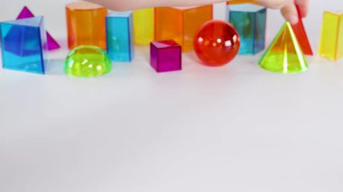 Bir el, hareketlerini ve düzenini gösteren, beyaz bir yüzeyde canlı üç boyutlu geometrik şekillerle etkileşir.