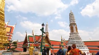 Turistler, Bangkok 'taki Wat Phra Kaew tapınak kompleksini gezerek, parlak gün ışığı altında süslü mimarisini yakalıyorlar.