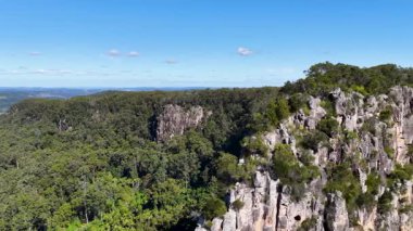 İnsansız hava aracı görüntüleri Nimbin Kayaları 'nın engebeli güzelliğini yakalar, yemyeşil ve çarpıcı kaya oluşumlarını açık mavi gökyüzü altında gösterir.