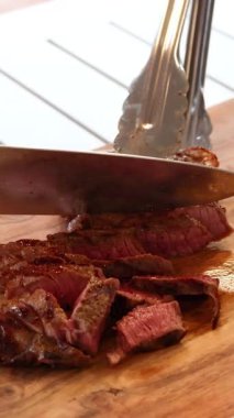 Bir bıçak, ahşap bir tahtada pişmiş bifteği dilimliyor. Doğal ışıkta sulu, taze eti vurguluyor.