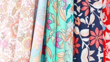 Doğal ışıkta sergilenen renkli kumaşlar, hareketli bir sokak pazarında karmaşık tasarımlar ve dokular sergiliyor.