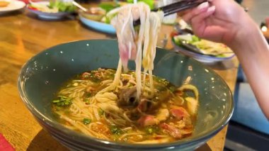 Çubuklar pirinçli erişteyi buharlı bir kaseden çıkarıp Bangkok 'taki bir restoranın canlı yemek atmosferini yakalıyor.