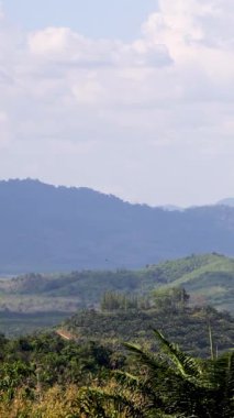 Parlak, parçalı bulutlu bir gökyüzünün altında geniş yeşil tepeler sergilenen sakin bir manzara, pürüzsüz bir döngü hareketiyle yakalanır.