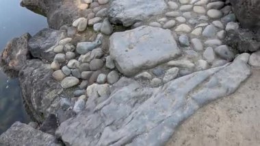 Bir su kütlesinin yanında çeşitli taşlar ve çakıl taşları.