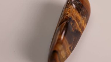 Bir kaplanın göz taşı beyaz bir yüzey üzerinde pürüzsüz döner, yumuşak ışık altında zengin kahverengi ve altın renklerini sergiler.