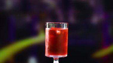 Bir Negroni kokteyli, bulanık bir arkaplan karşısında portakal dilimiyle süslenir, canlı renkler ve gevşemiş bir ruh hali vurgulanır.