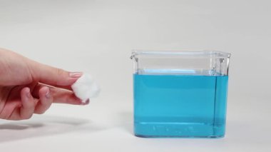 Bir el, bir pamuk yumağını mavi sıvıyla dolu temiz bir kabın içine yerleştirir ve yüzme kabiliyetini gözlemler.