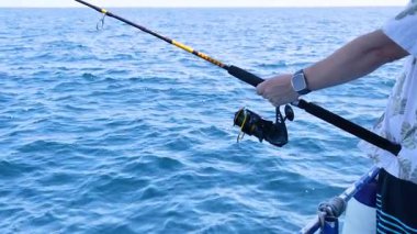 Tayland, Phuket 'te bir teknede balık tutan biri. Sahne, okyanusu, oltayı ve sakin atmosferi yakalar.