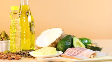 Sıcak ışıklandırmalı ahşap bir yüzey üzerinde yağlar, fındıklar ve avokadolardan oluşan canlı bir düzen.