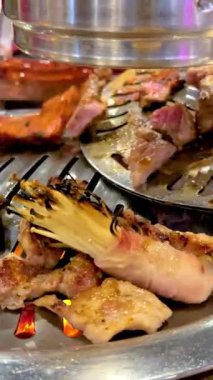 Izgara et ve mantarlar canlı bir Bangkok ortamında Kore barbekü ızgarasında cızırdıyor.