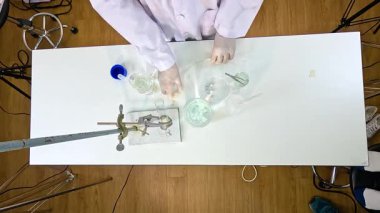 Bir bilim adamı, beyaz bir masada laboratuvar malzemesi kullanarak bakır karbonatla termal bozunma deneyi yürütüyor.