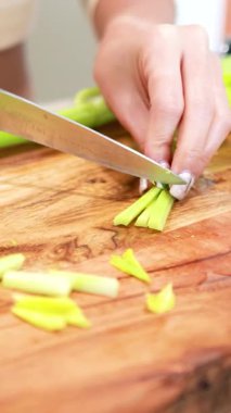 Ahşap bir tahtanın üzerinde kereviz doğrayan becerikli eller. Parlak ışıklandırma, taze malzemeleri ve bıçak işini ön plana çıkarıyor.