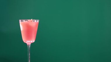 Yeşil ekran arka planında bardakta pembe bir kokteyl. Sabit kamera, canlı renkler ve minimalist kompozisyon