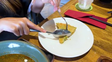 İyi aydınlatılmış bir restoran ortamında ahşap bir masada gevrek bir Vietnam karidesini dilimleyen eller.