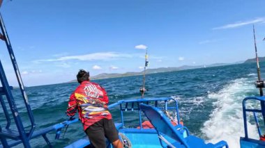 Tayland, Phuket 'te hareket halindeki bir tekneden balık avlıyor. Parlak gün ışığı, berrak gökyüzü ve okyanus dalgaları canlı, dinamik bir sahne yaratır.