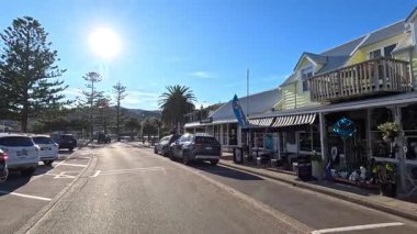 Akaroa 'nın güneşli caddelerinde manzaralı bir gezinti, dükkanları, park edilmiş arabaları ve açık mavi gökyüzünün altındaki rıhtım manzaralarını yakalamak.