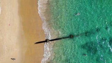 Kalabalık bir Phuket plajında turkuaz sularla güneşli bir günün tadını çıkaran turistleri görüntüleyen hava görüntüleri.