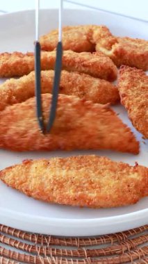 Parlak doğal ışık altında, beyaz bir tabakta maşayla, çıtır çıtır tavuk kanatları düzenleniyor.