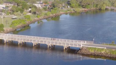 Havadan çekilen görüntüler sakin suların üzerindeki sakin bir köprünün parlak gün ışığında yemyeşil bir alanla çevrili olduğunu gösteriyor.