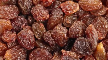 Kuru üzümler, yumuşak ışıklandırma altında desen ve renk varyasyonlarını vurgulayan ayrıntılı bir makro görünümde bir yığın içine dökülür