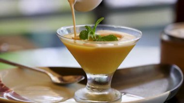 Bir Tayland tatlısının üzerine yakın plan krema dökülüyor, zengin dokuyu ve canlı sunumu vurguluyor.