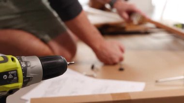 Eller masadaki matkap kullanarak mobilyaları birleştirir. Parlak ışıklandırma odaklanmış etkinliği vurgular