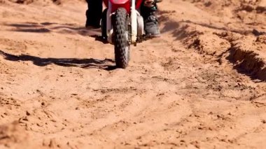 Motosikletçi zorlu kumlu arazide sürüyor.