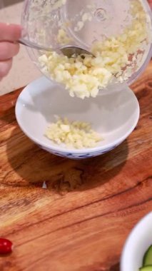 Sarımsak doğranır ve parlak mutfak ışıklarının altındaki tahta bir tahtanın üzerindeki bir kaseye aktarılır.