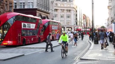 Kırmızı çift katlı otobüslerin yanından geçen bisikletçi