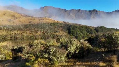 Güneşin doğuşunda bir dron tarafından yakalanan, sisli ve güneşli, sakin bir dağ manzarasının havadan görüntüsü.