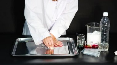 Bir bilim adamı, laboratuvar ortamında çeşitli sıvılar kullanarak metal tepside temizlik teknikleri gösteriyor.