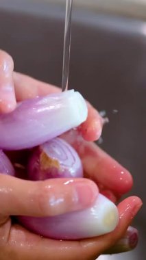 Mutfak ortamındaki bir su deresinin altında soğanları durulayan ellerin yakın çekimi.