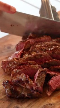 Bir şef ahşap bir tahtada lezzetli bir bifteği ustalıkla dilimliyor, etin hassasiyetini ve zengin rengini vurguluyor.