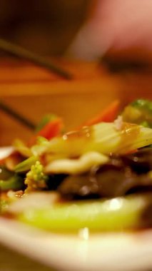 Yemek çubukları, sıcak bir restoran ortamında ısıtılmış tabaktan canlı kızarmış sebzeleri nazikçe kaldırır.